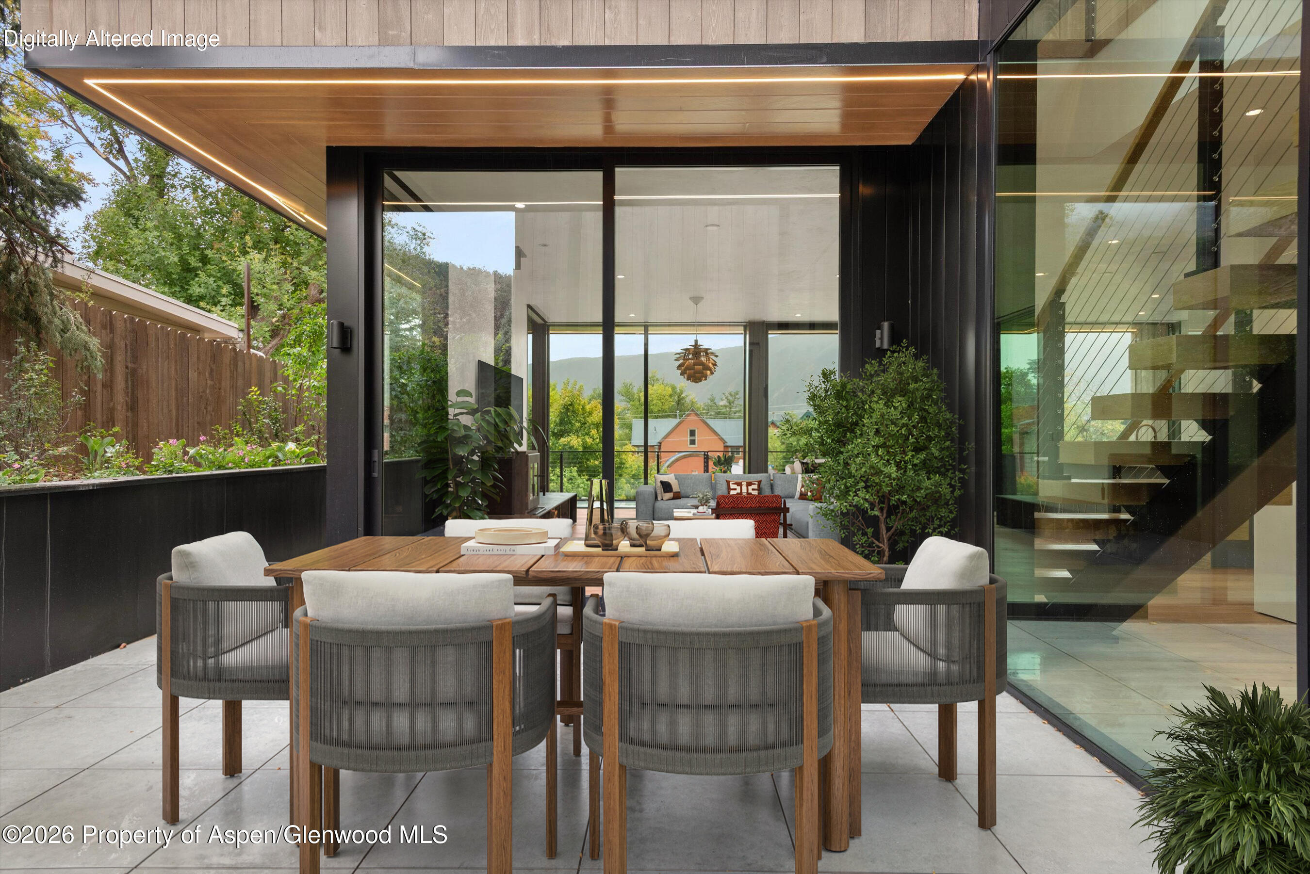 Covered patio dining area with a long wood table, glass walls, and mountain views.