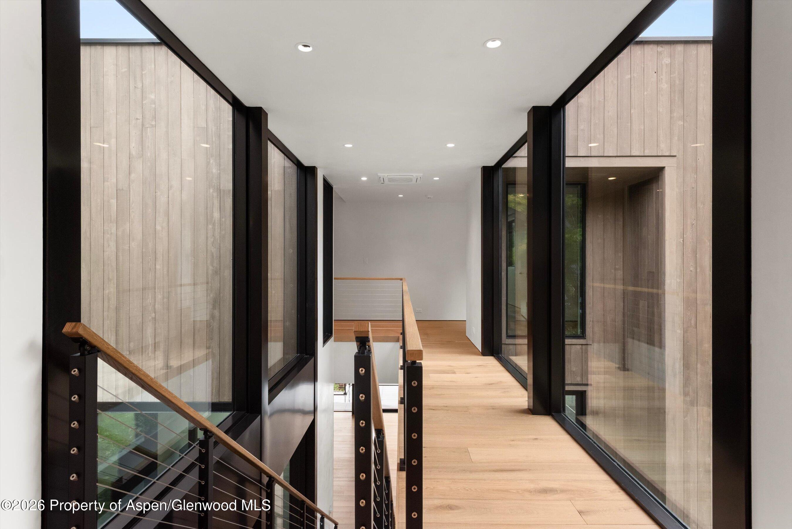Unfurnished upper-level hallway with a wood floor, glass walls, and a view down to the staircase.