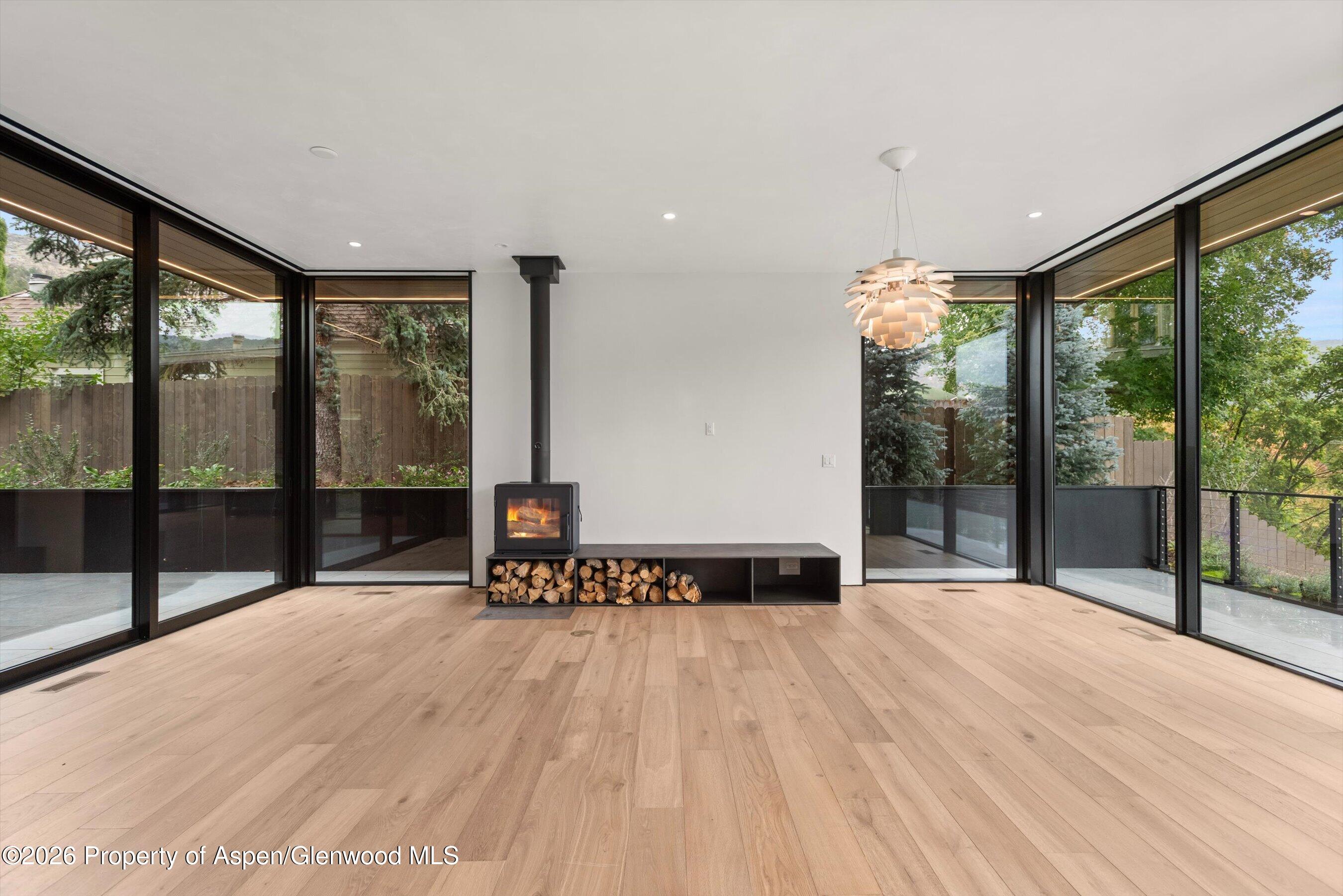 Modern living room with a wood-burning stove, built-in log storage, and floor-to-ceiling windows.