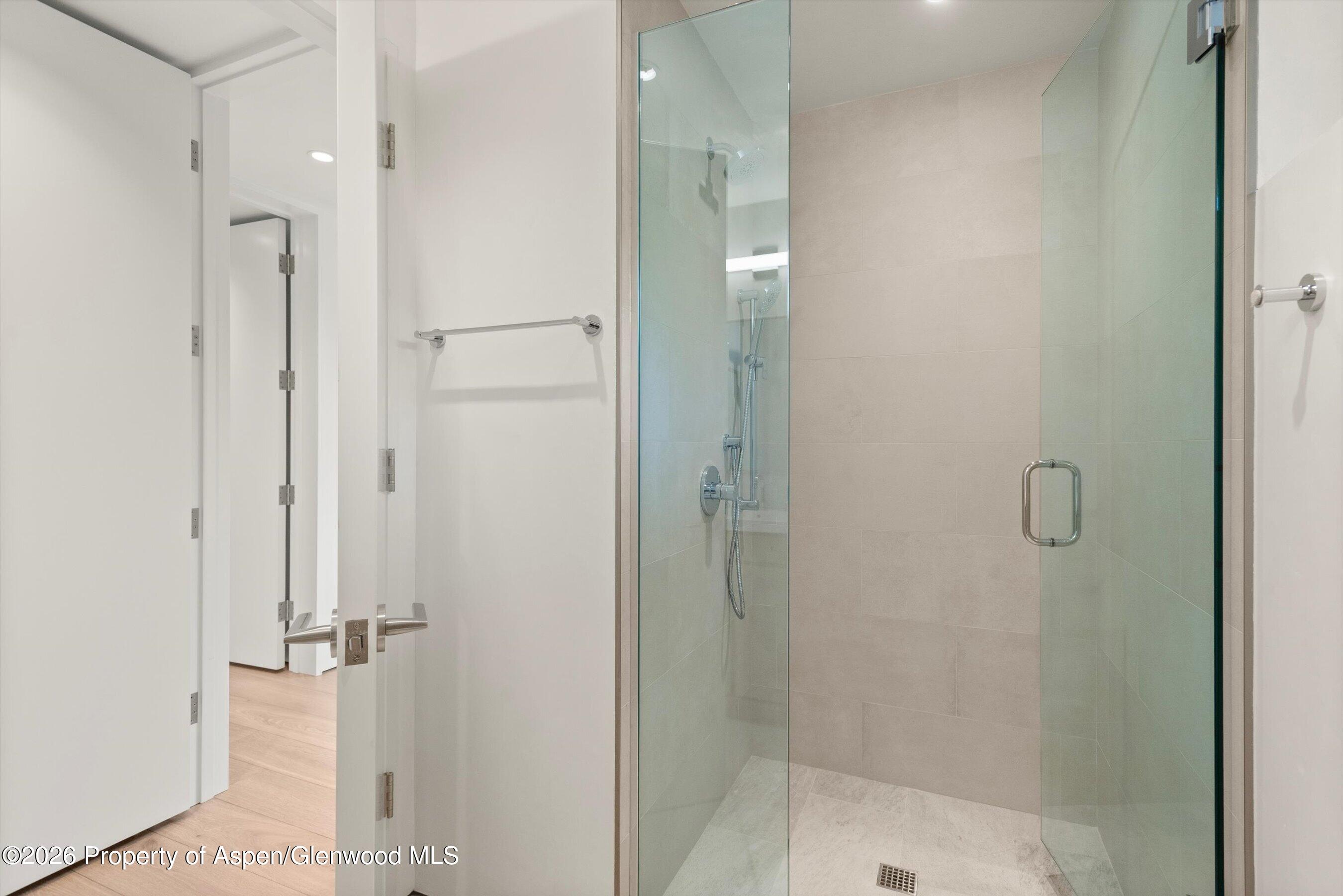 Modern walk-in shower with glass doors, beige tile, chrome fixtures, and a pale stone floor.