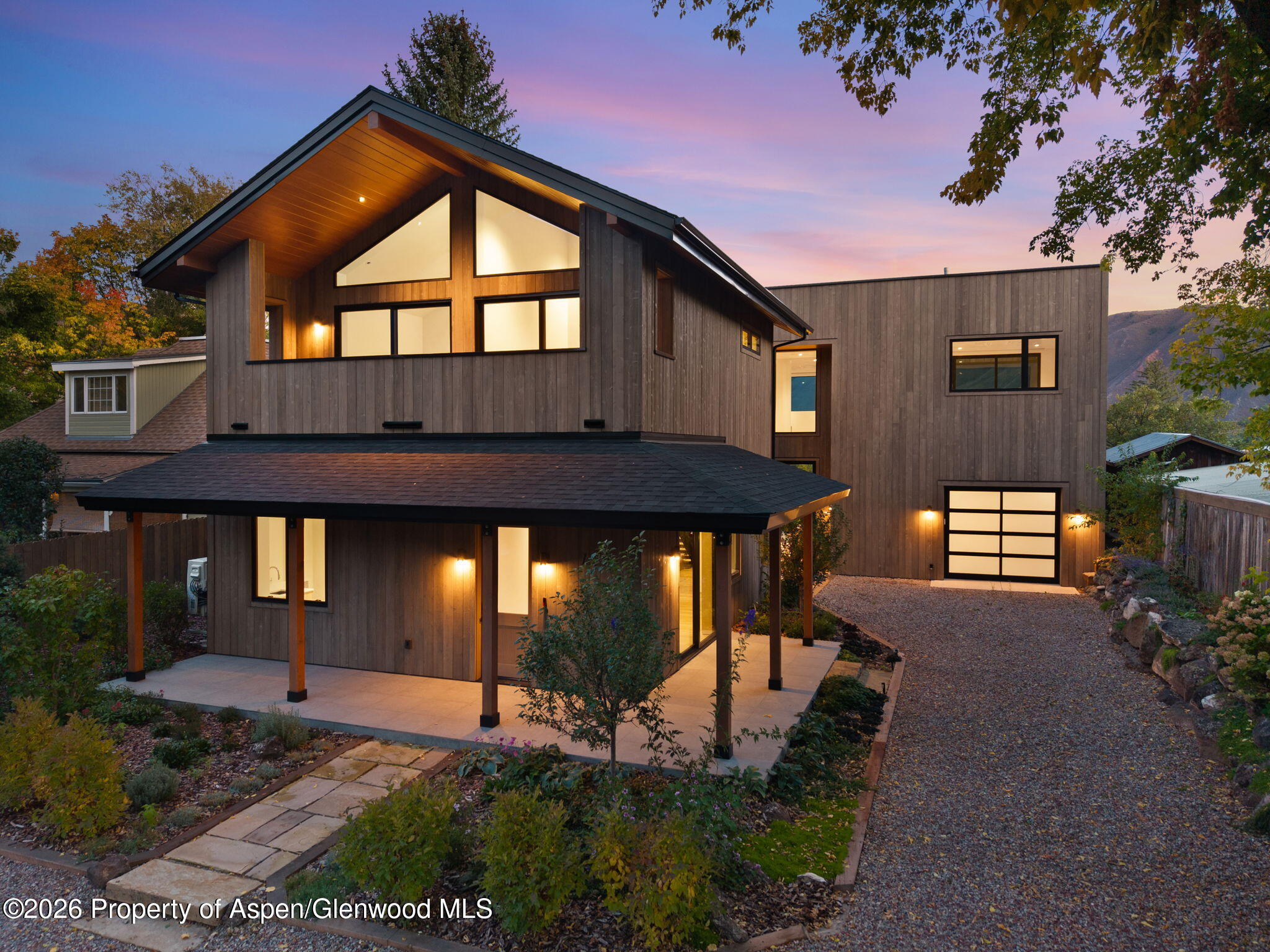 Modern wood-clad home with a covered patio and glowing windows at dusk.