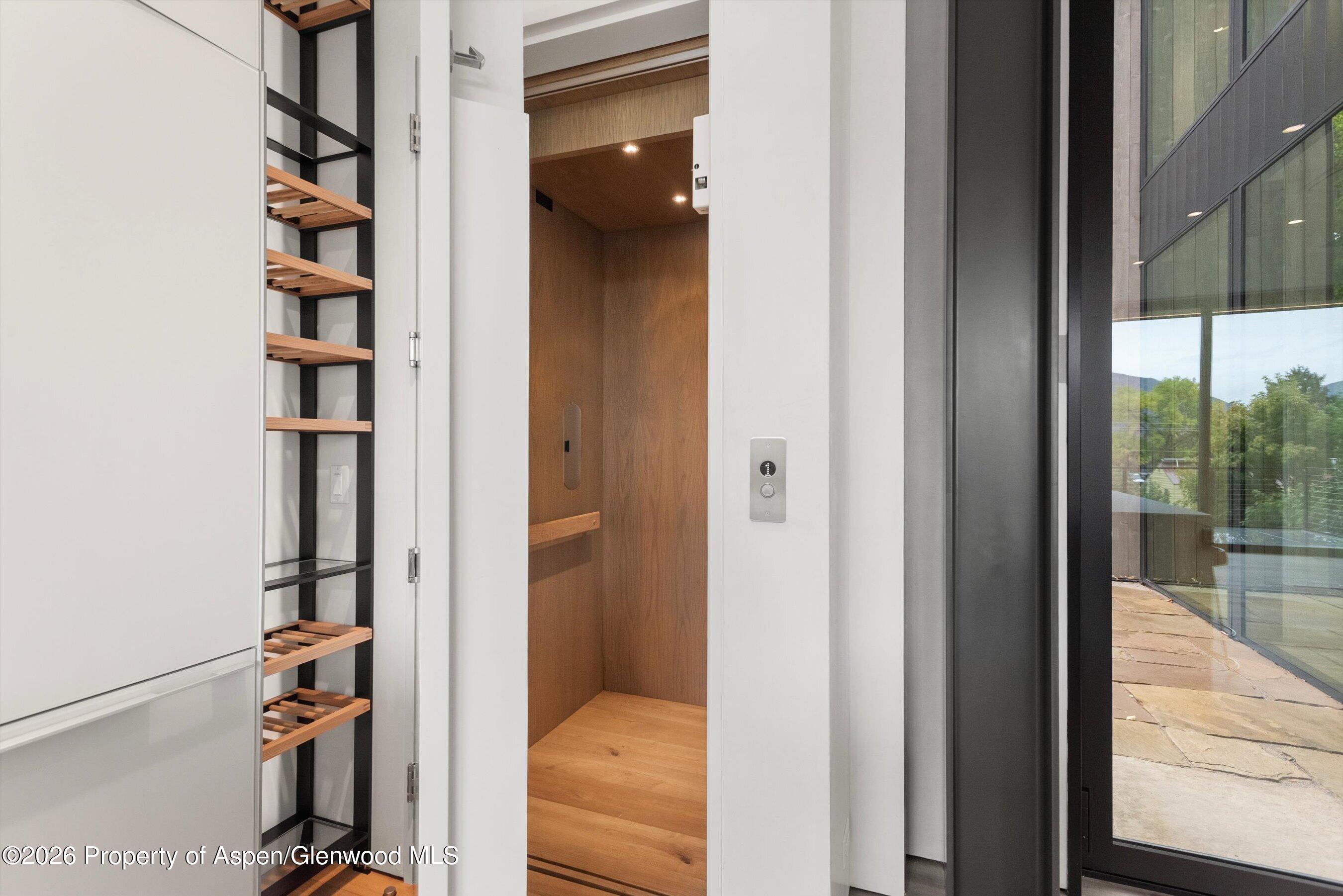 Open wood-paneled elevator beside built-in shelving, with a glass-walled terrace visible outside.