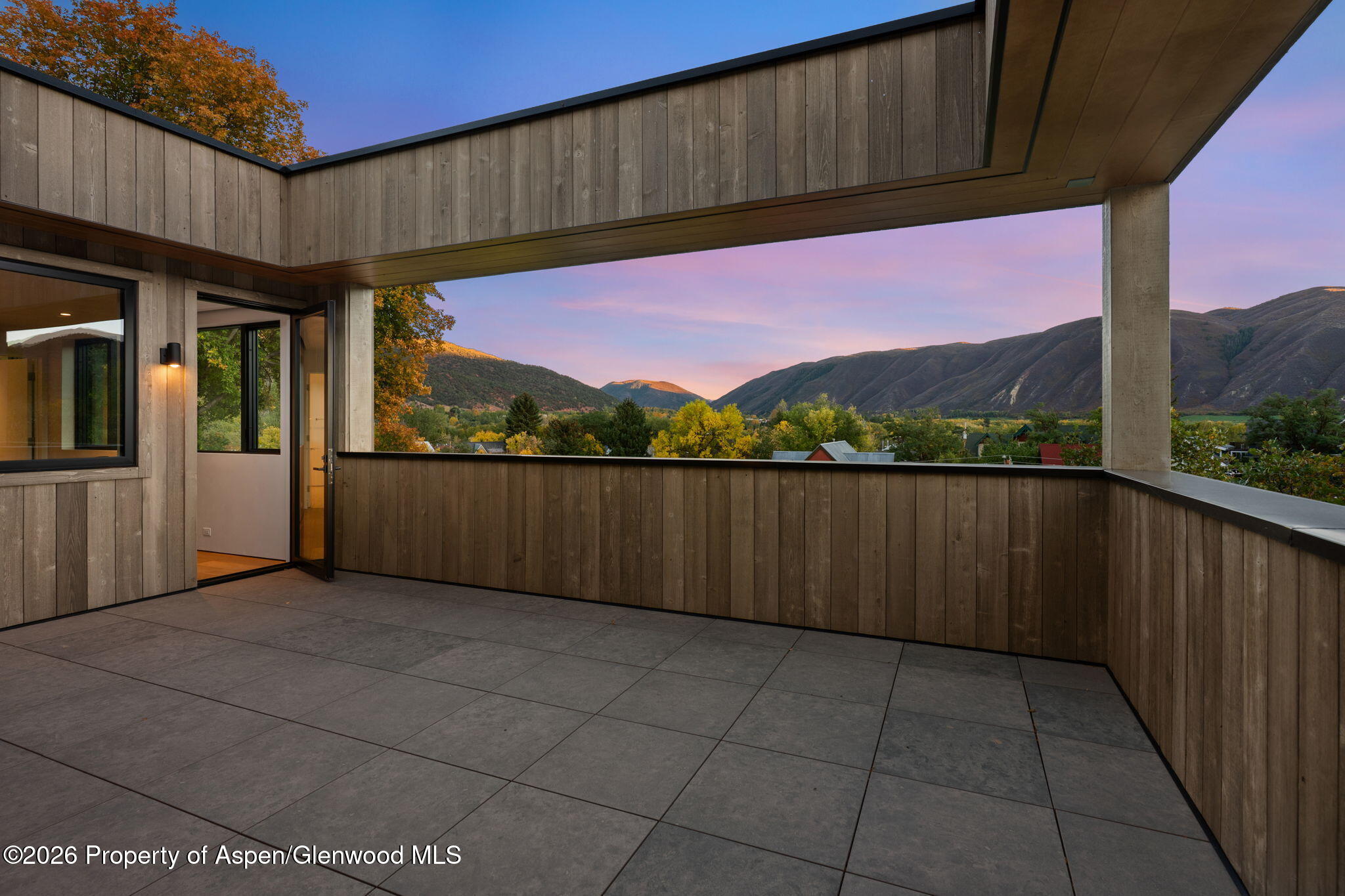 Covered terrace with tiled flooring and wood paneling overlooking an autumn mountain valley at dusk.
