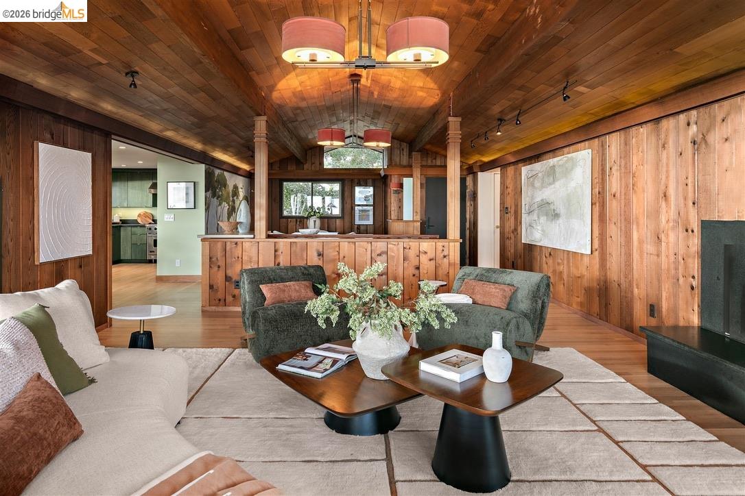 Wood-paneled living room with a vaulted ceiling, staged sofas, and an open view into the kitchen.