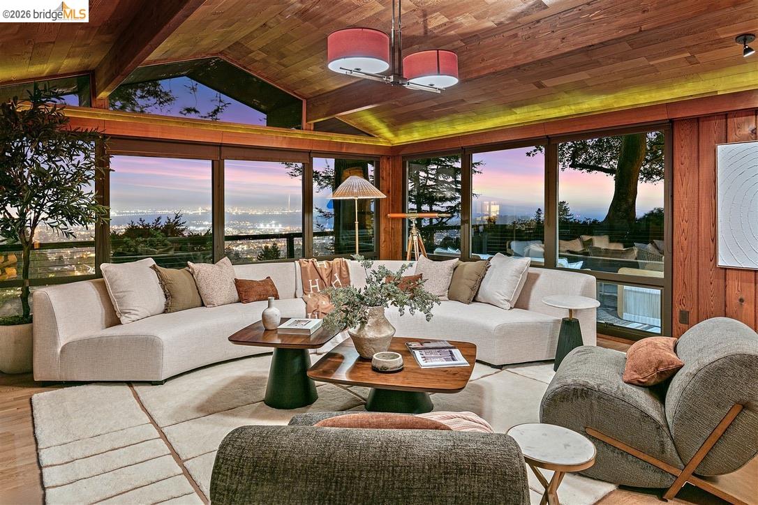 Living room with a wood-plank ceiling, sectional sofa, and panoramic dusk views of the city and water.