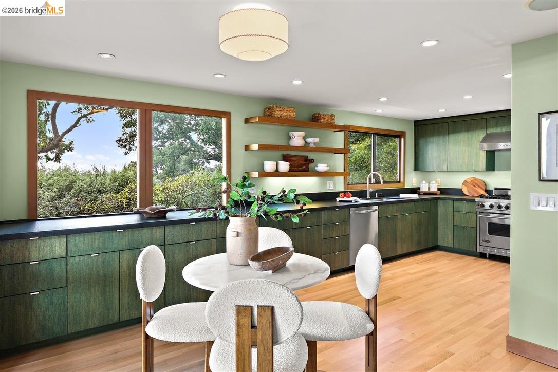 Kitchen with dark green cabinetry, open shelves, and large windows overlooking greenery.