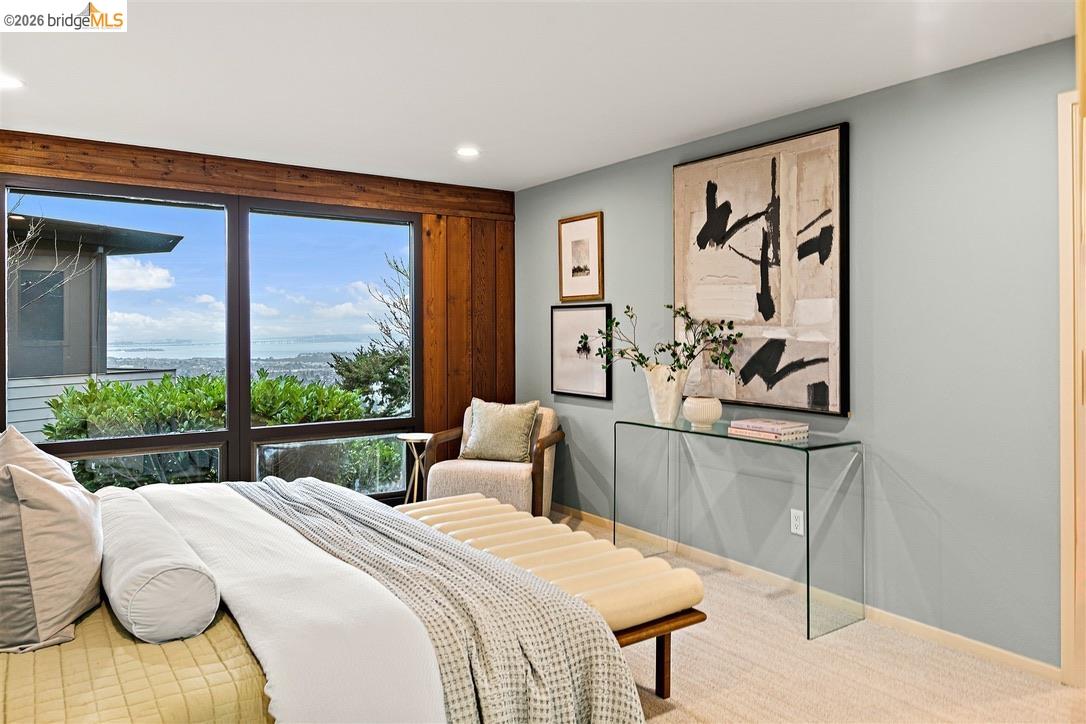 Bedroom with wood-trimmed windows overlooking the water and a bed with an upholstered bench.