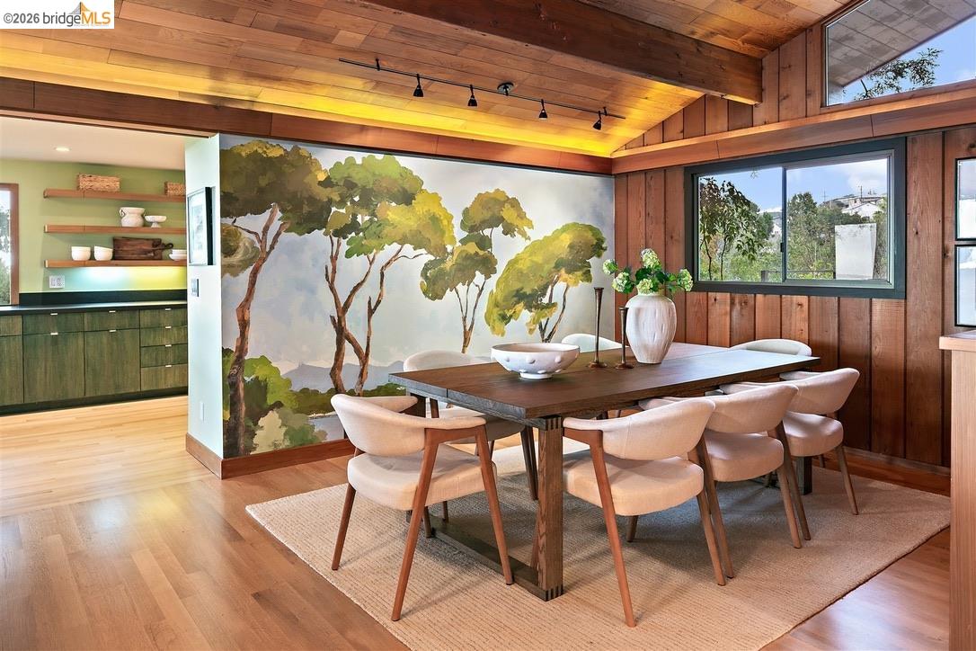 Dining room with a painted tree mural, wood ceiling, and dark table surrounded by pale upholstered chairs.