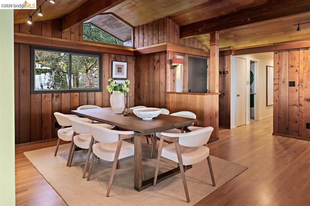 Dining room with a long table, white chairs, wood-paneled walls, and a vaulted timber ceiling.