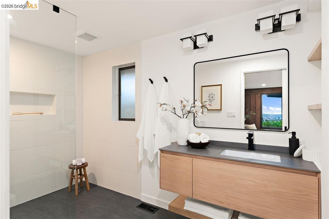Modern bathroom with a glass-enclosed shower, wood floating vanity, and large black-framed mirror.