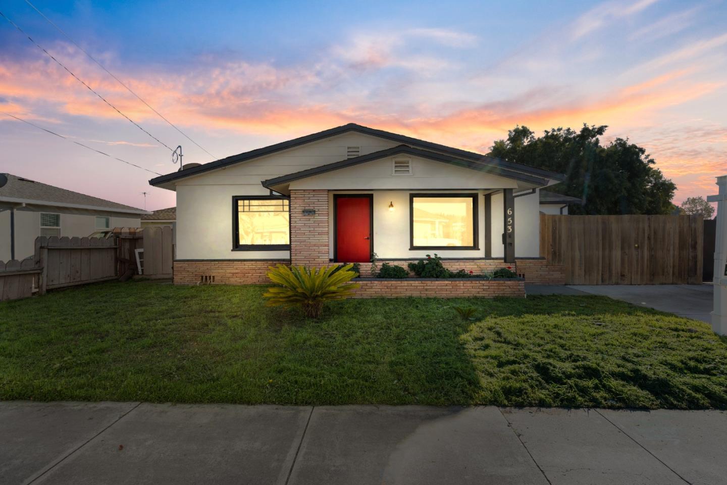 Single-story home with a red front door, brick accents, and a front lawn at sunset.
