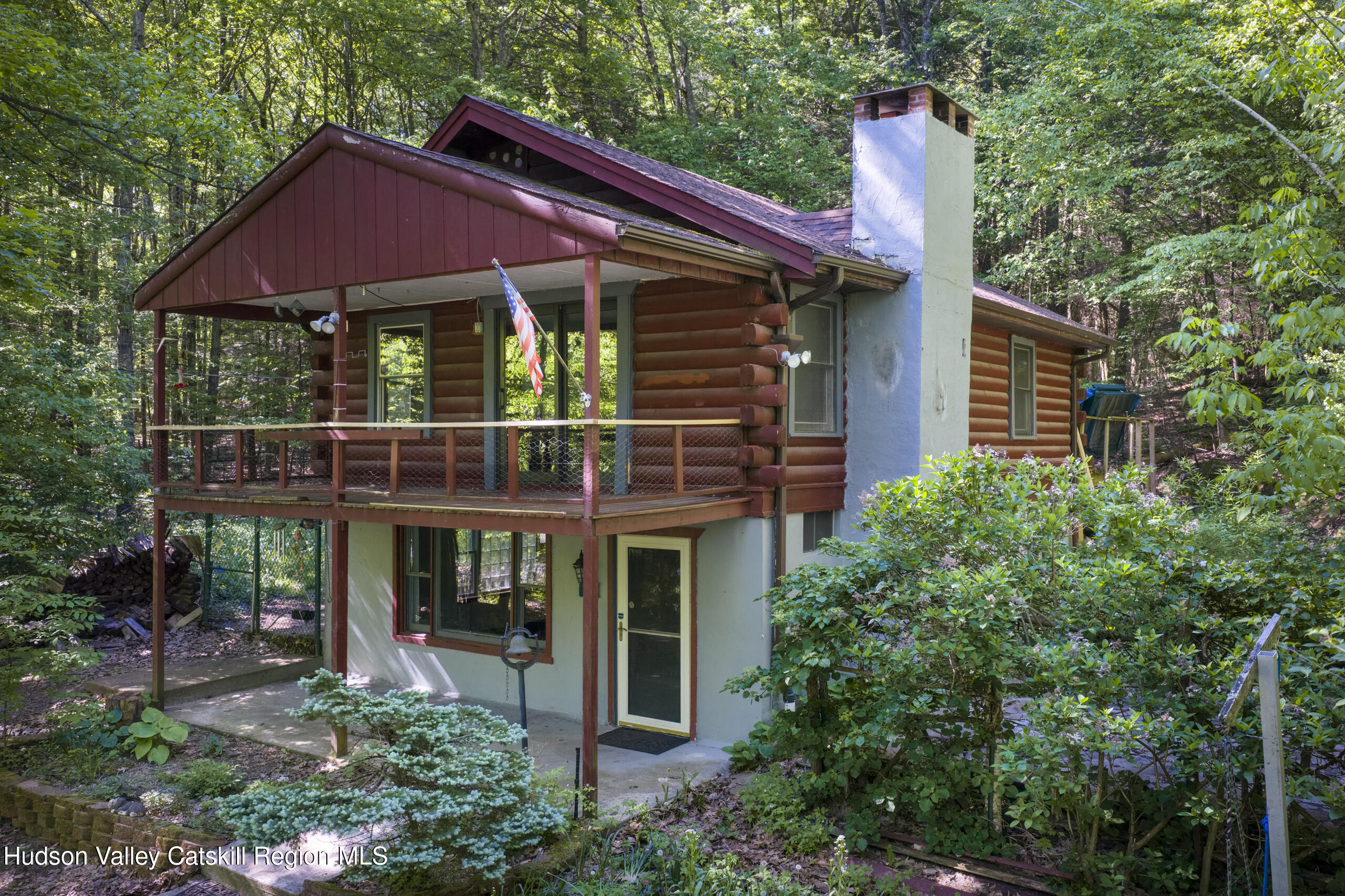 Woodland cabin with a covered porch, white chimney, and American flag.