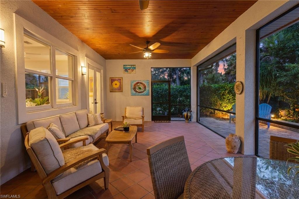 Furnished lanai with a wood ceiling and wide windows overlooking a garden at dusk.