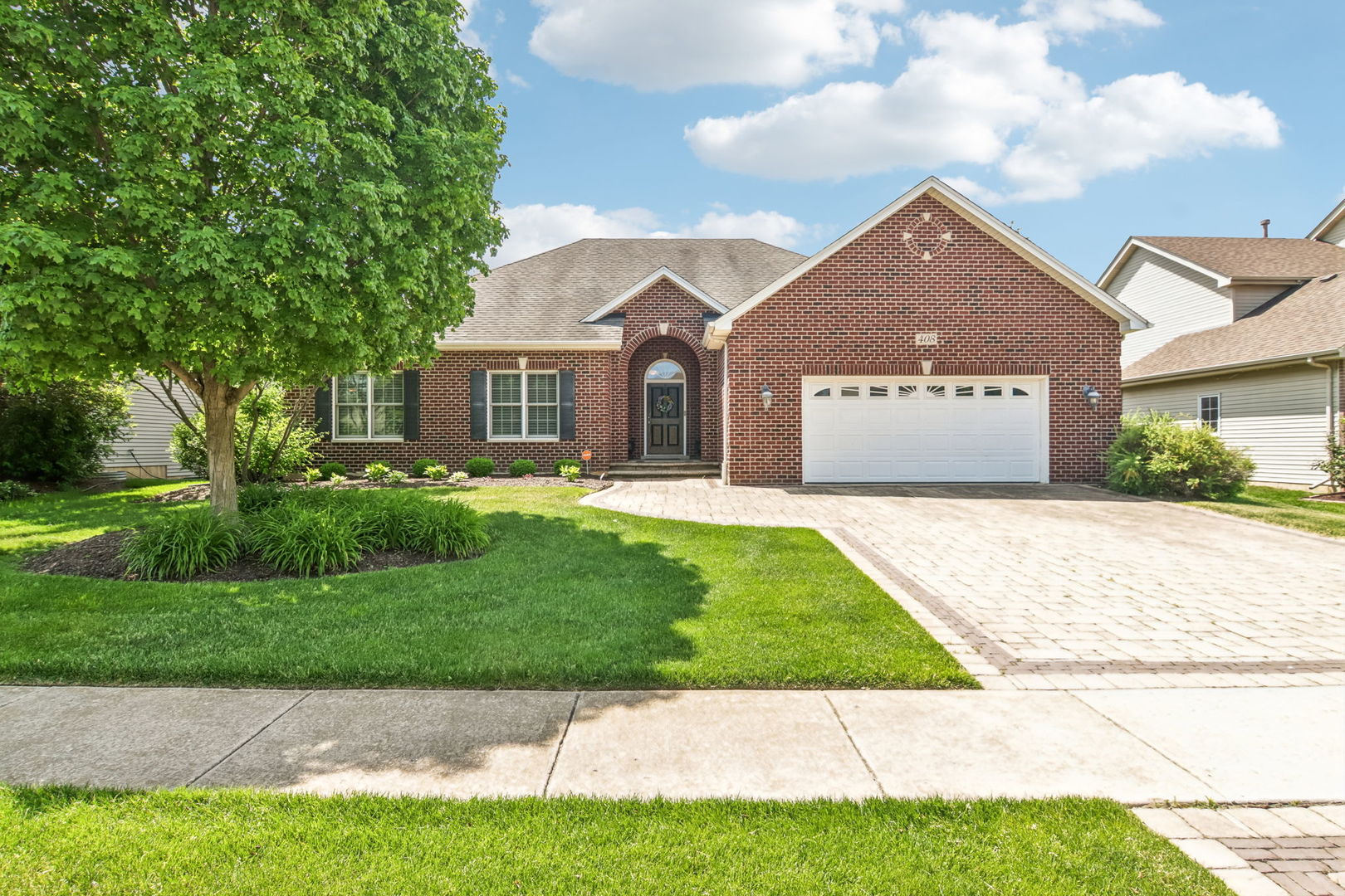 Red brick home with an arched entry, white garage, paver driveway, and mature front yard.