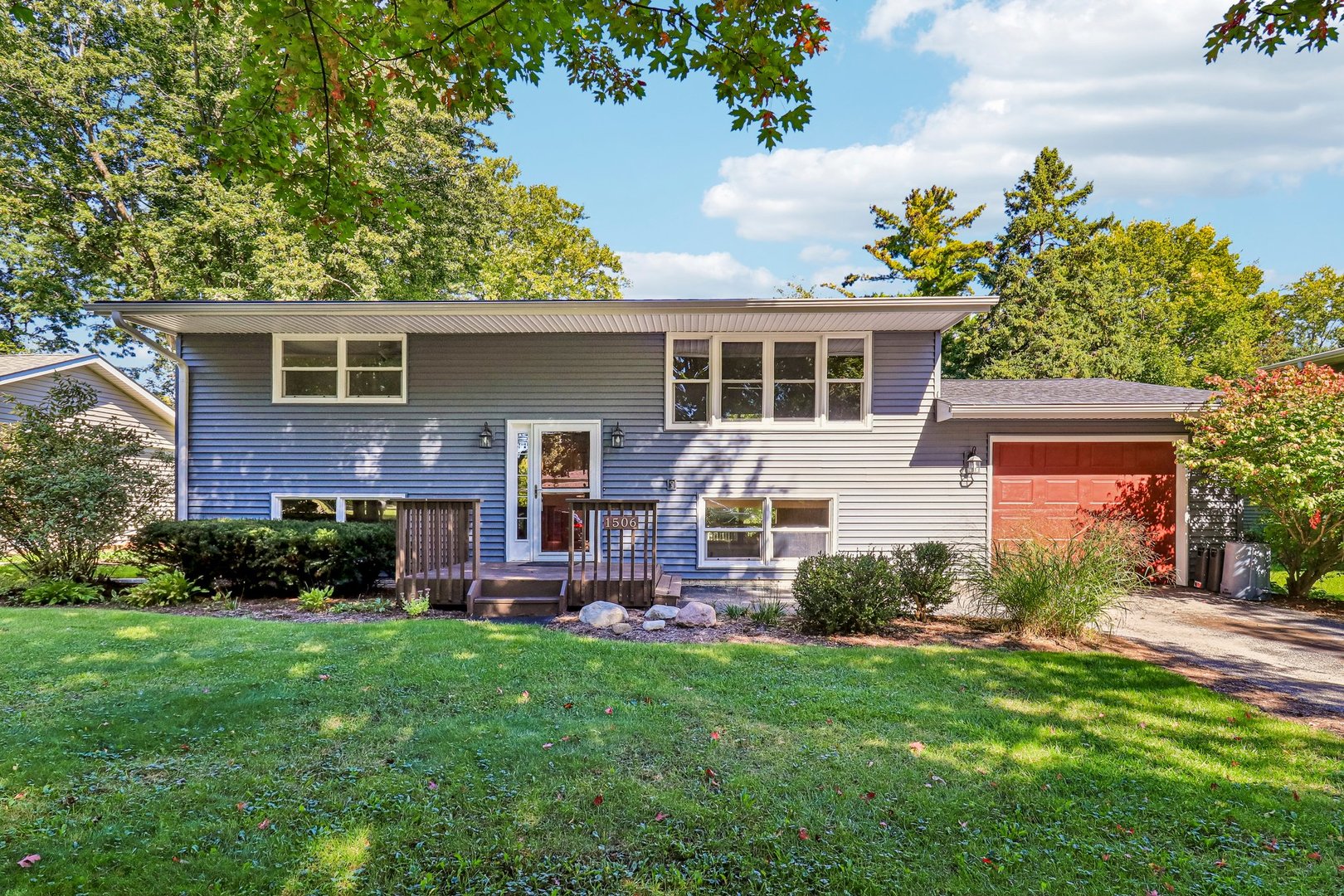 Gray split-level house with a red garage door, small front porch, and leafy yard.