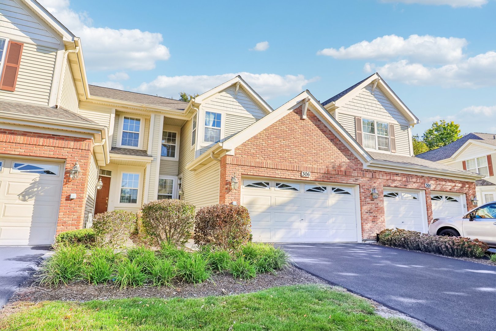 Adjoining two-story homes with brick accents, white garage doors, and landscaped shrubs.