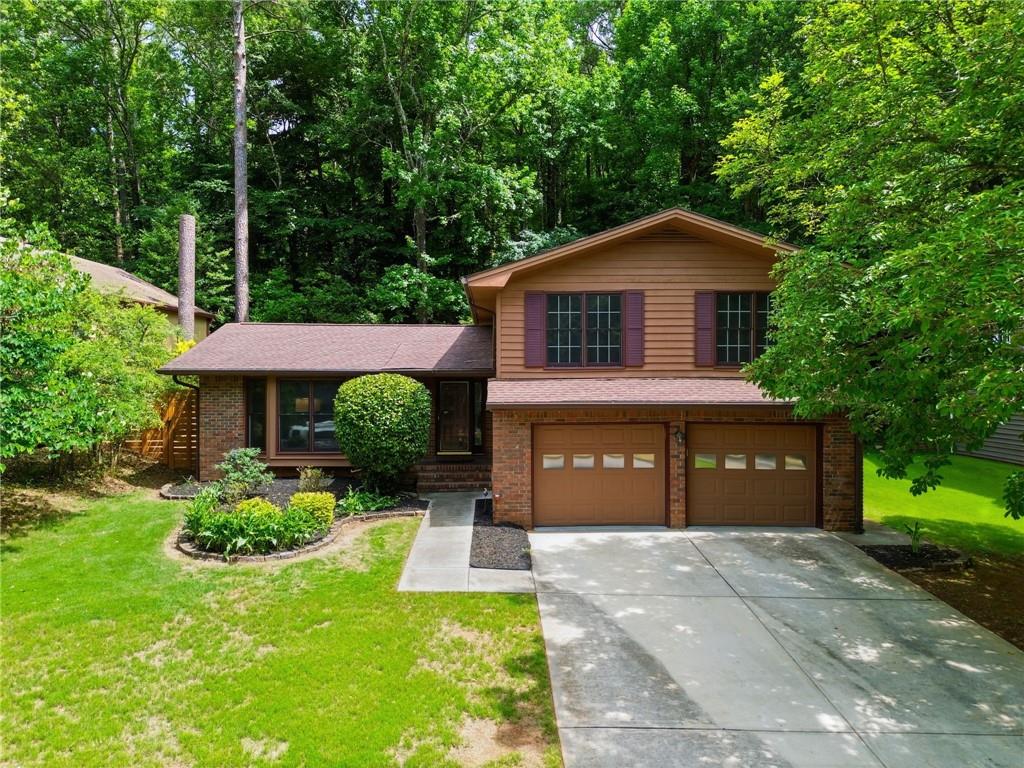 Two-story brown-and-brick house with a two-car garage, mature trees, and a broad concrete driveway.