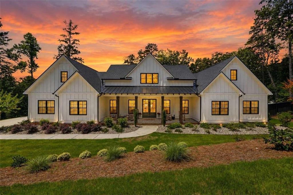 White multi-gabled home with a covered porch and glowing windows at sunset.