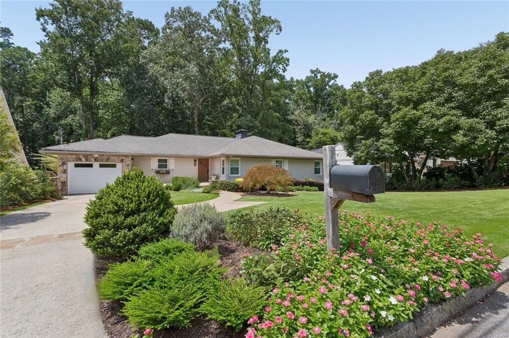 Single-story home with an attached garage, driveway, mailbox, and flower-filled front garden.