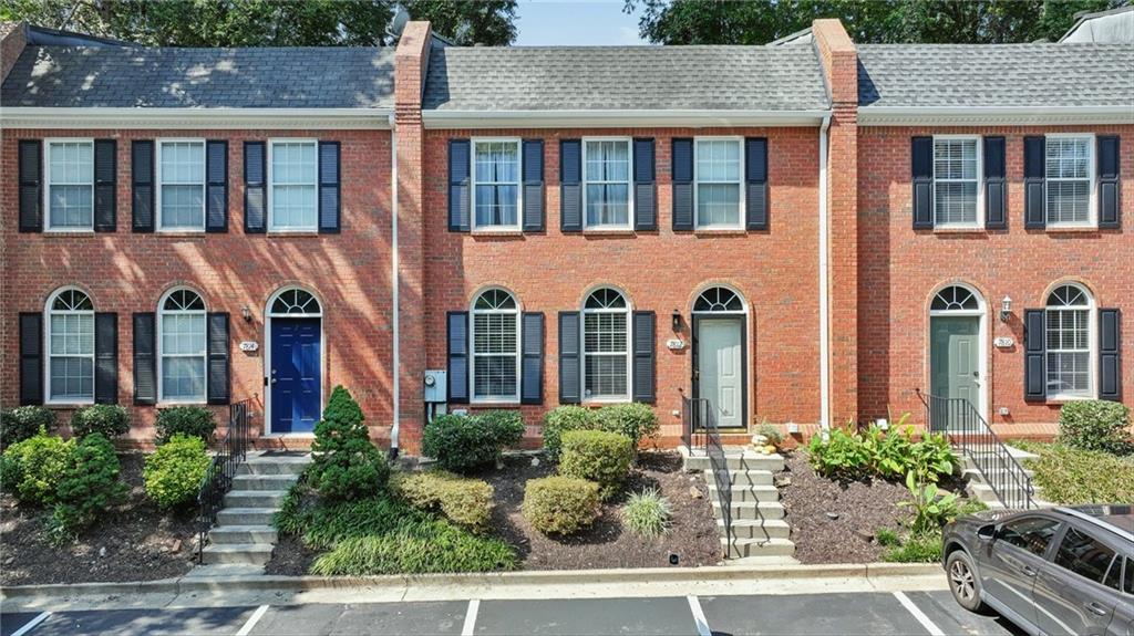 Brick townhome exterior with black shutters, arched windows, landscaped entry, and front parking.