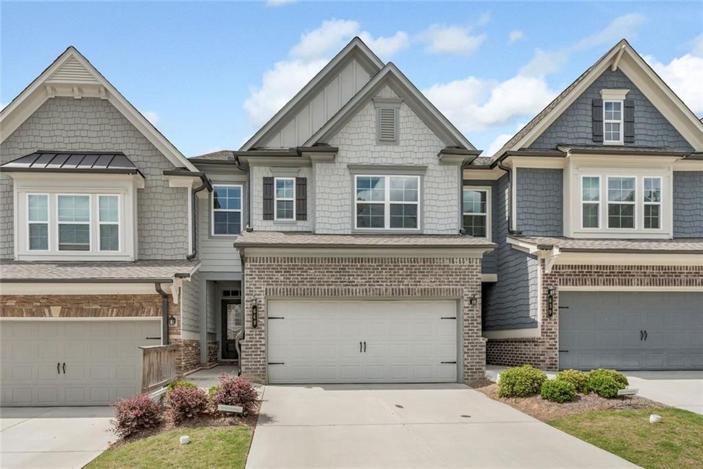 Gray two-story attached home with shingle siding, brick accents, and a double garage.