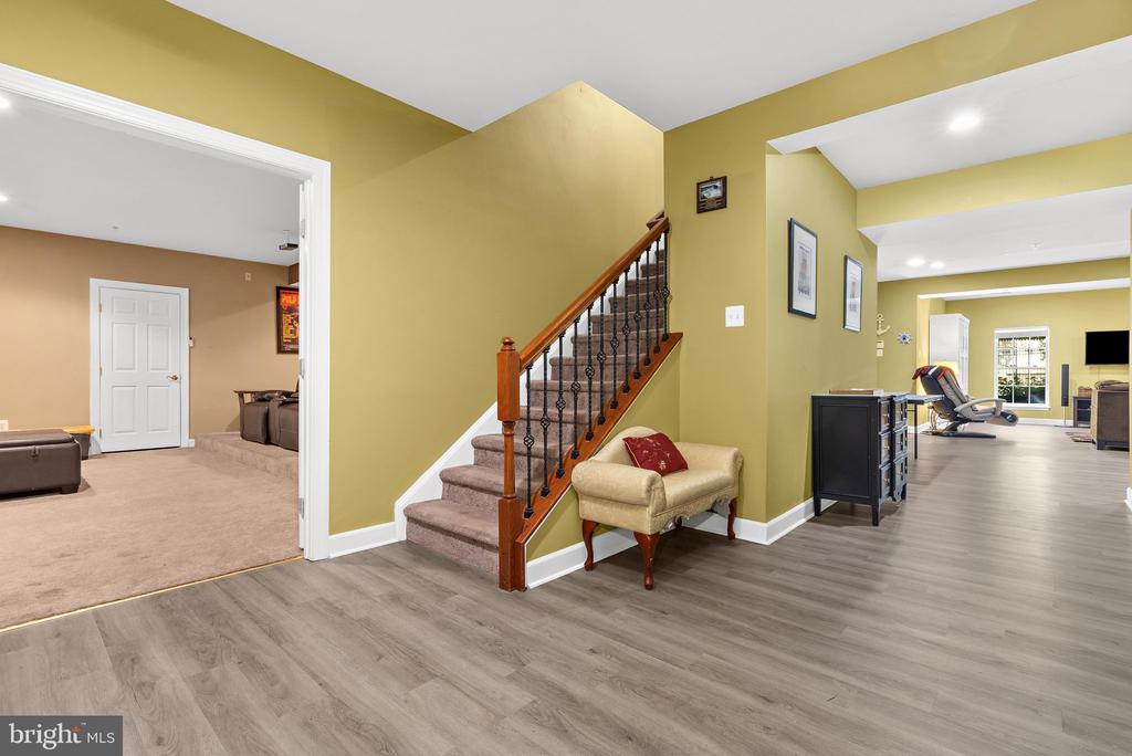 Entry hall with an oak staircase, gray wood-look floors, and open doorways to furnished living areas.