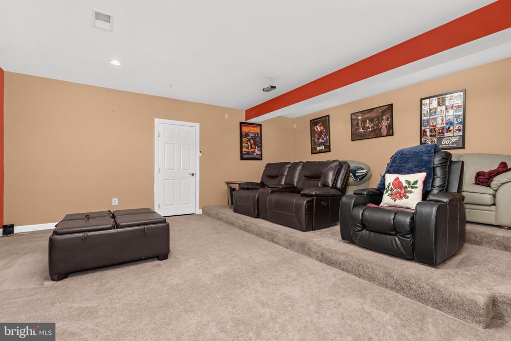 Furnished media room with tiered carpet, leather theater seats, and framed movie posters.