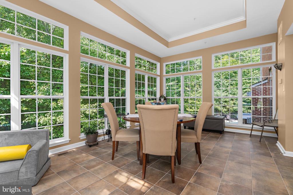 Furnished sunroom with a dining table, expansive windows, and views of green trees.