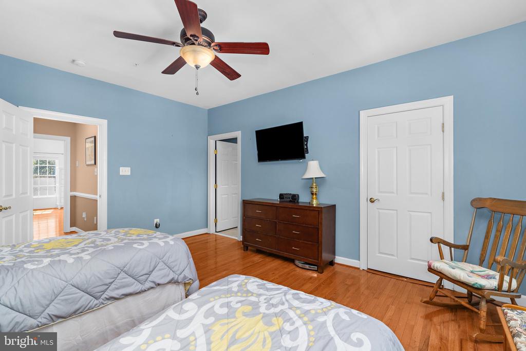 Bedroom with blue walls, hardwood floors, floral bedding, a dresser, and a wooden rocking chair.