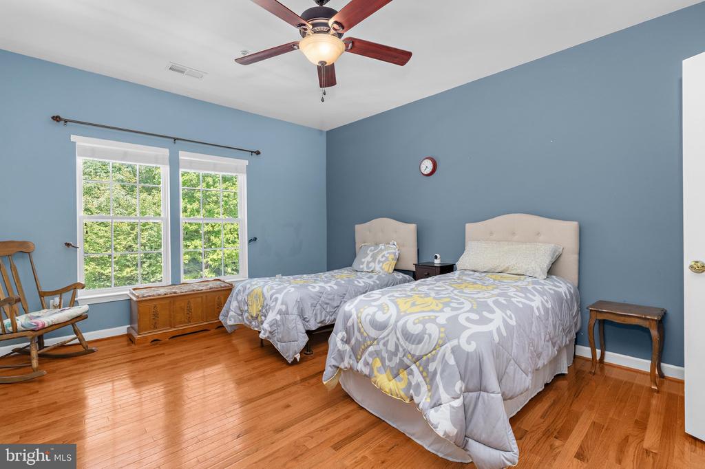 Bedroom with two beds, blue walls, hardwood floors, and large windows overlooking greenery.