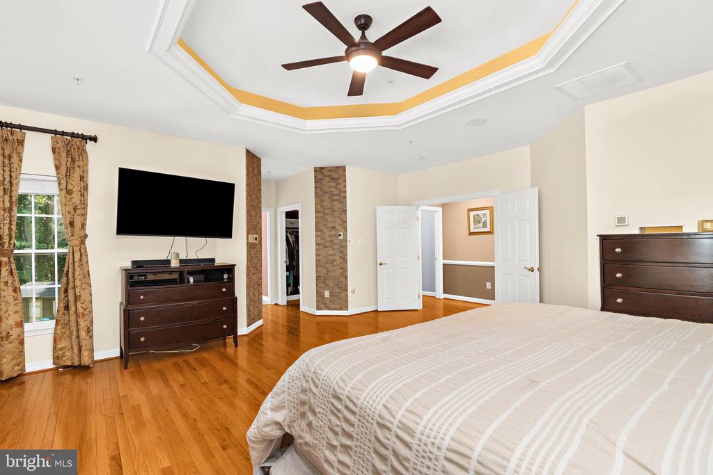 Furnished bedroom with a tray ceiling, ceiling fan, hardwood floors, and dark wood furniture.