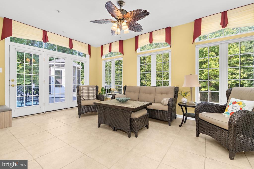 Furnished sunroom with wicker seating, tall windows, and French doors overlooking trees.