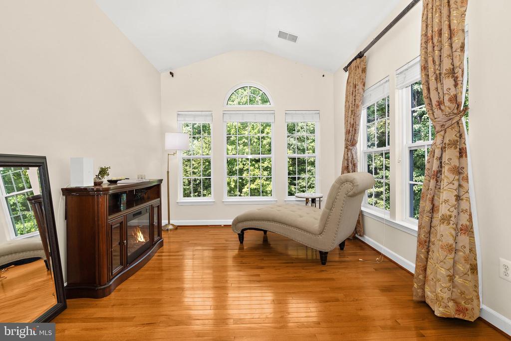 Sitting room with a cream chaise, hardwood floors, fireplace cabinet, and tall windows overlooking trees.