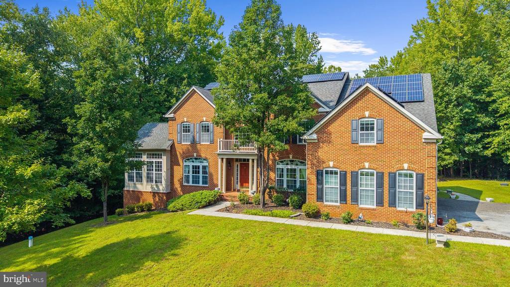 Red brick house with rooftop solar panels, landscaped lawn, and mature trees.