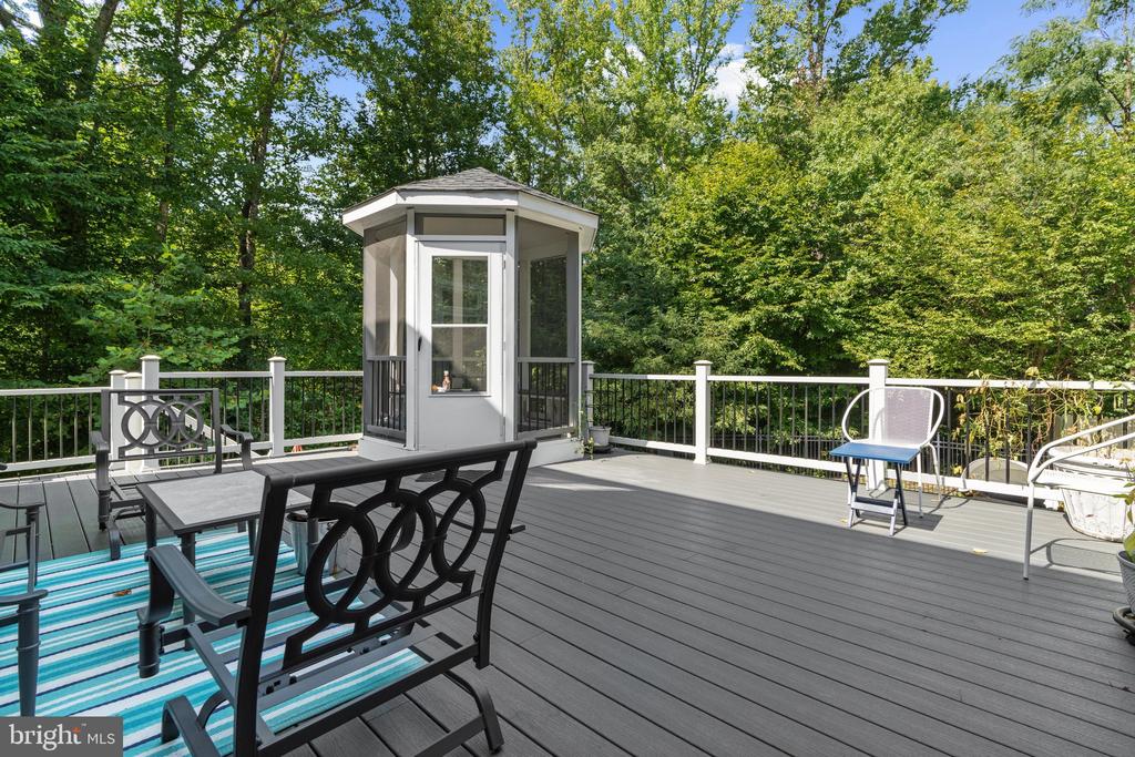 Furnished gray deck with an enclosed gazebo and wooded surroundings.