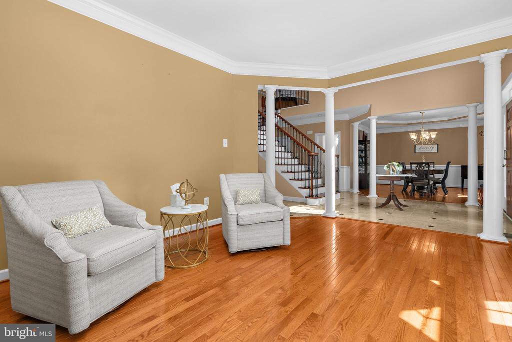 Living room with cream armchairs, hardwood floors, white columns, and an open staircase.