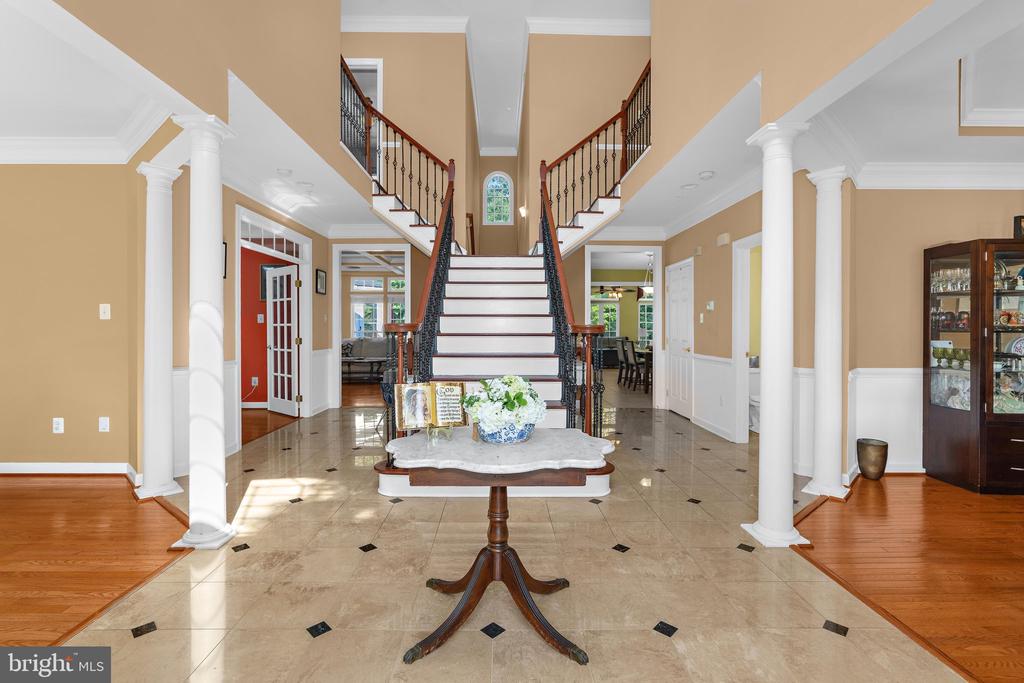 Grand foyer with a central staircase, marble tile, white columns, and a console table.