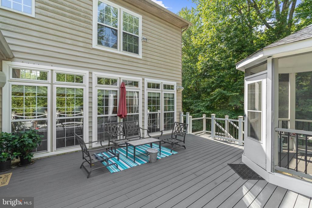 Furnished deck with black patio seating, a blue striped rug, and wooded surroundings.