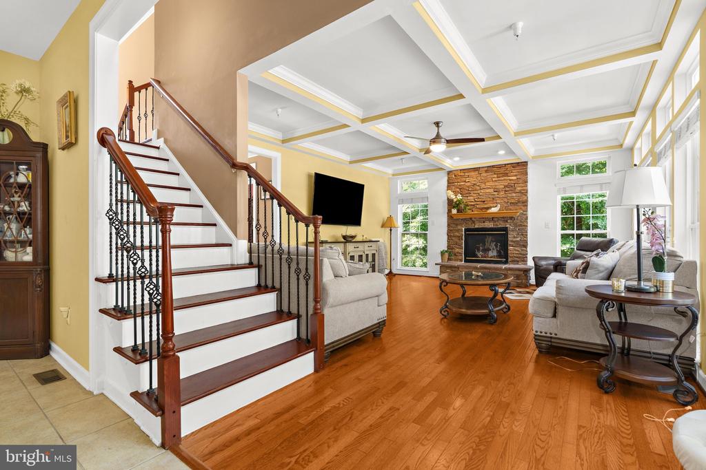 Living room with a sweeping staircase, coffered ceiling, and stone fireplace.