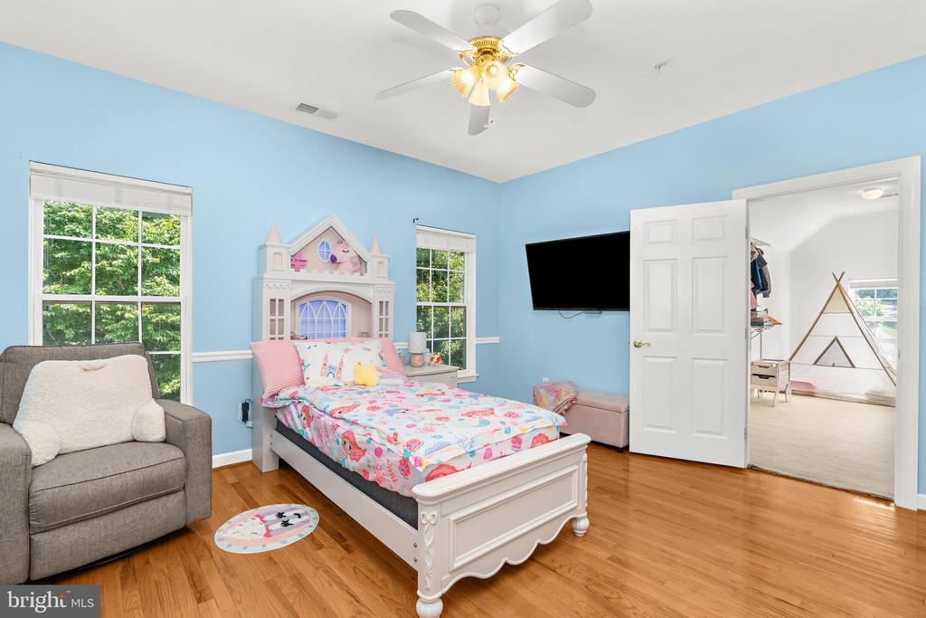 Bedroom with an ornate white bed, colorful bedding, blue walls, and hardwood floors.