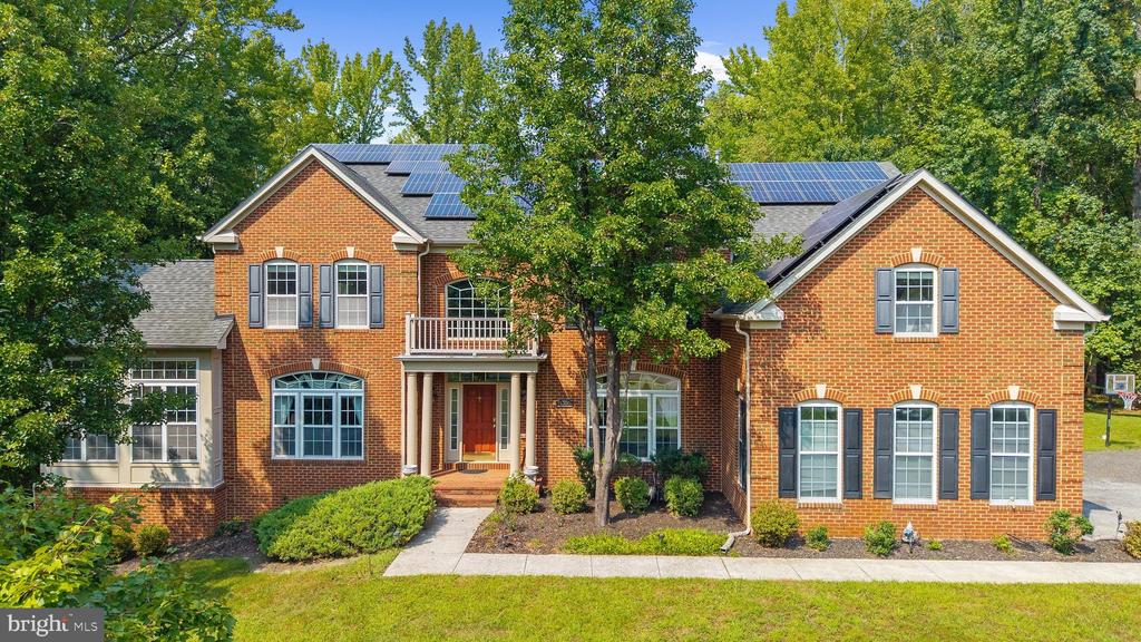 Two-story red-brick house with solar panels, a front balcony, and mature trees.
