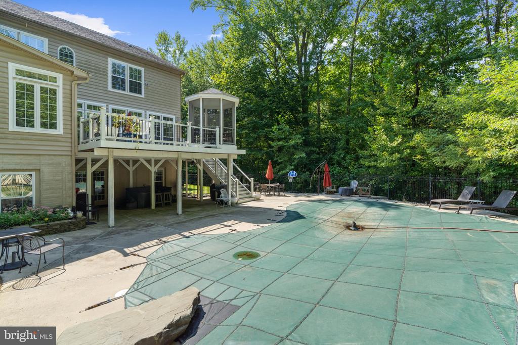 House rear deck and gazebo beside a covered swimming pool, patio furniture, and wooded yard.