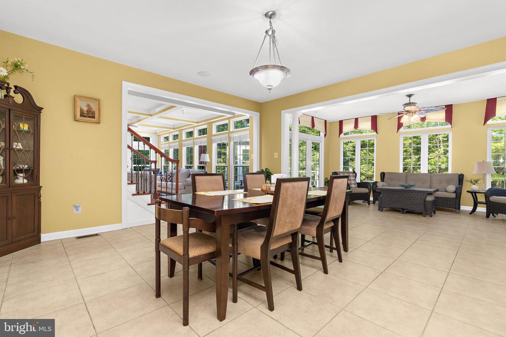 Dining room with a dark wood table, opening to a bright window-lined sitting area.