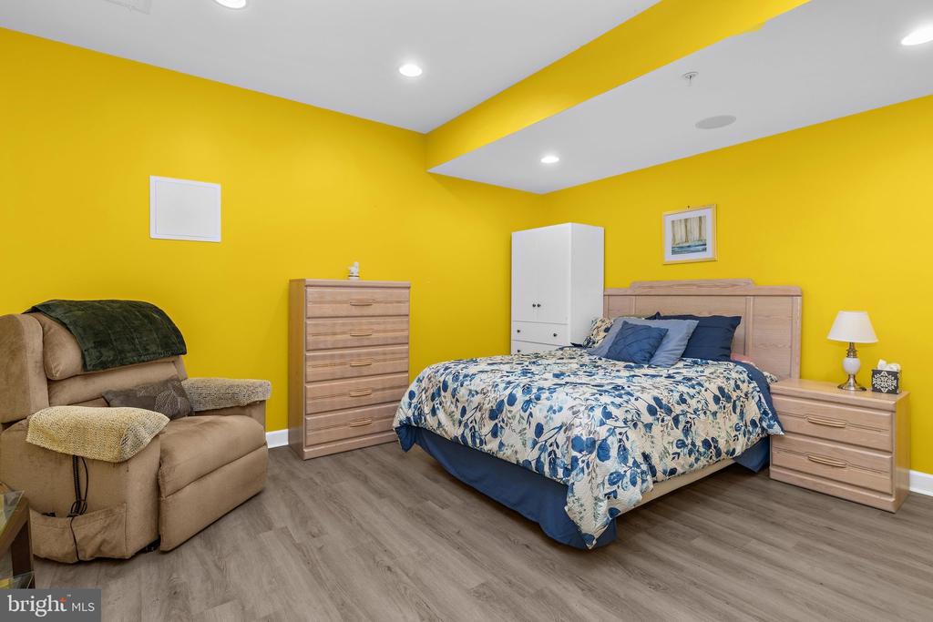 Bedroom with bright yellow walls, a floral bedspread, light wood dressers, and a tan recliner.