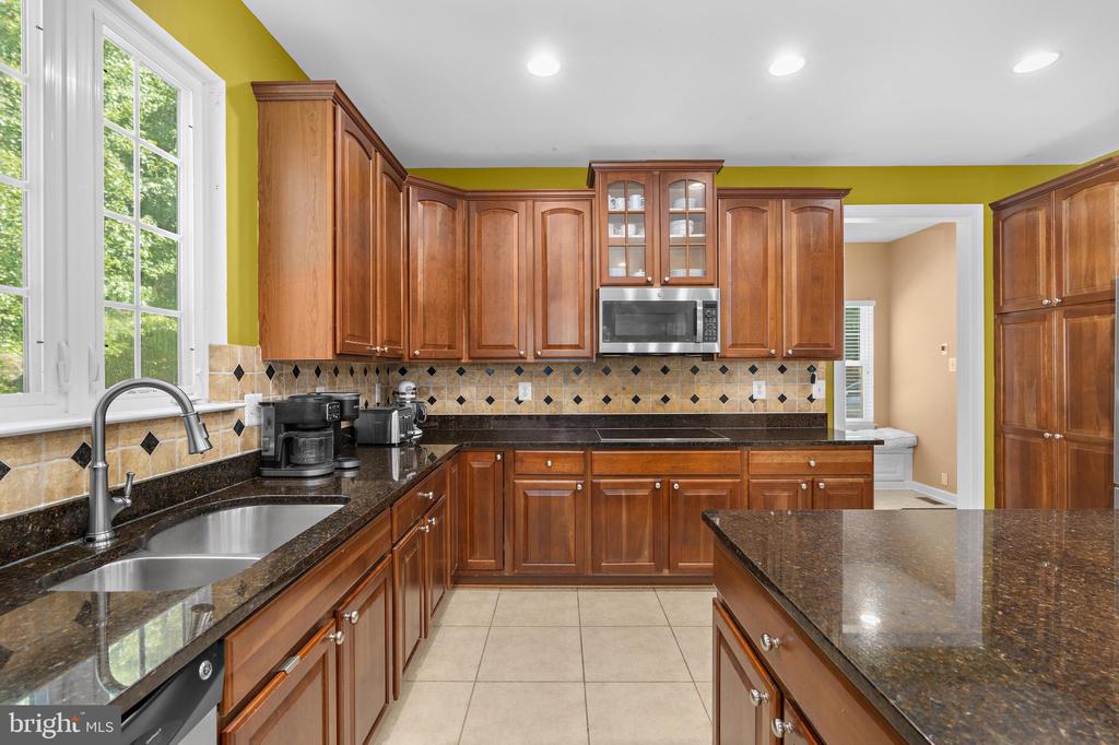 Kitchen with warm wood cabinets, dark granite counters, a large island, and a tiled backsplash.