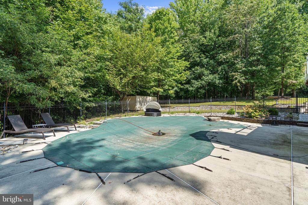 Swimming pool with a green safety cover, lounge chairs, and a wooded, fenced yard.