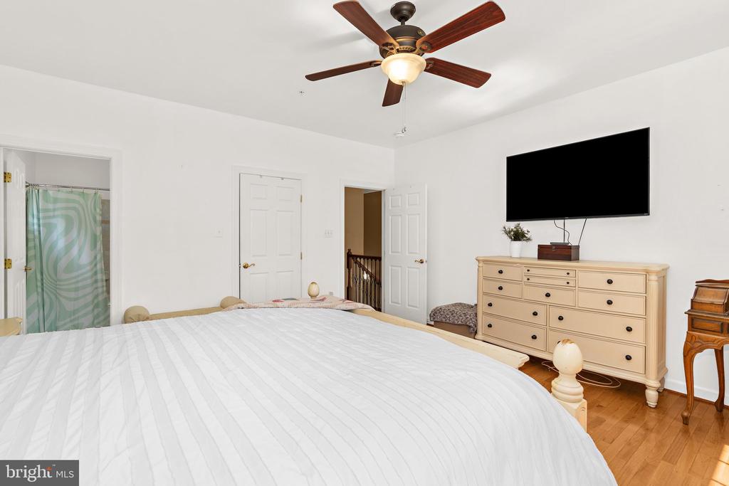 Bedroom with a large bed, ceiling fan, and dresser beneath a wall-mounted television.