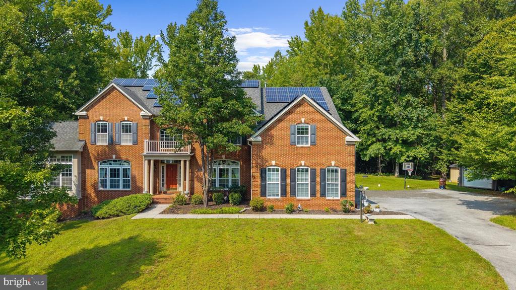 Red-brick two-story home with rooftop solar panels, a broad lawn, and a wooded setting.