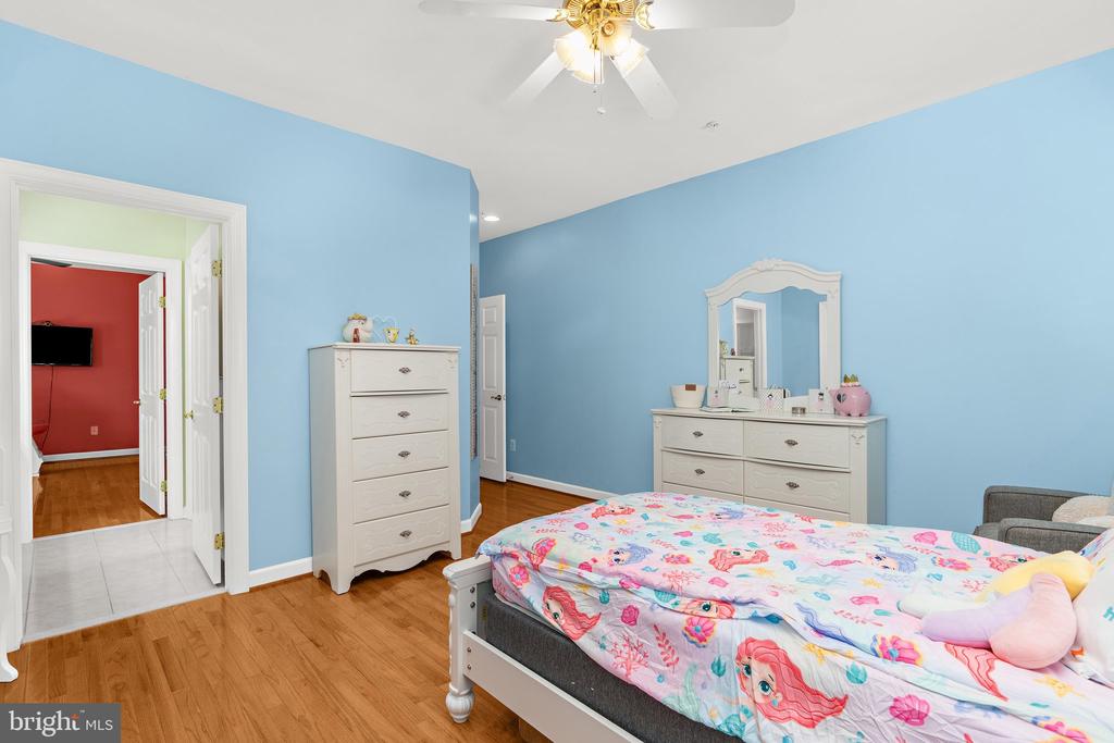 Blue bedroom with colorful floral bedding, white dressers, hardwood floors, and a ceiling fan.