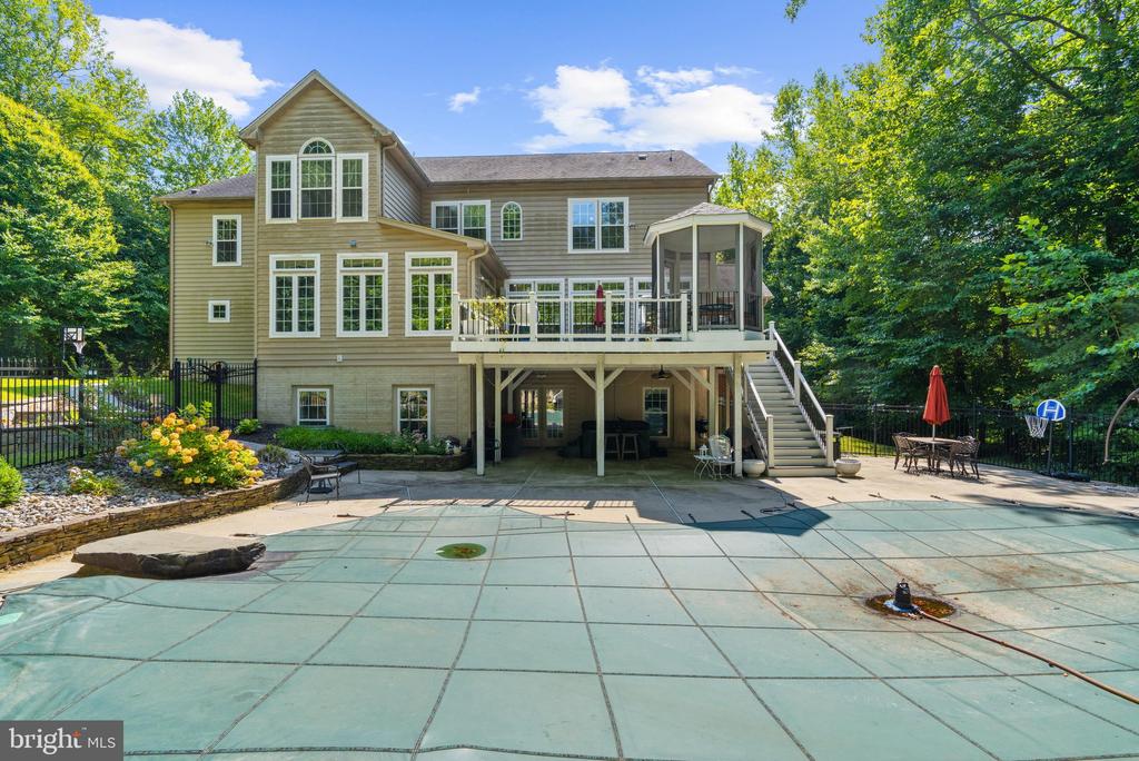Rear of a two-story home with a raised deck overlooking a large pool and wooded yard.